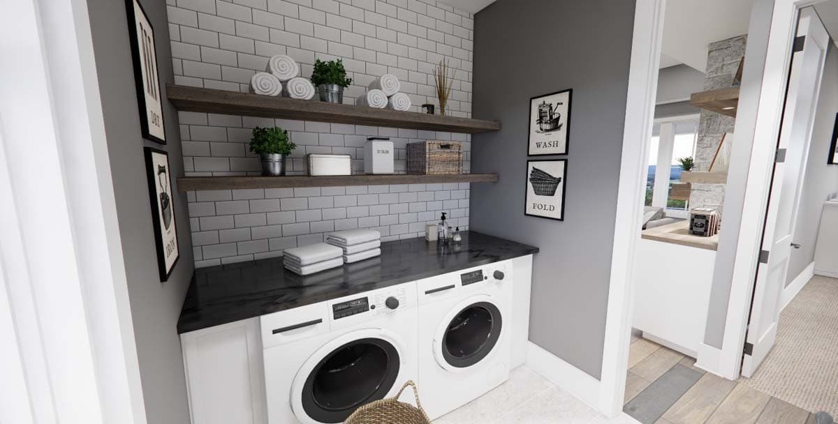 Laundry room with white washer and dryer, dark countertop, open shelving with subway tile backsplash, and framed art.