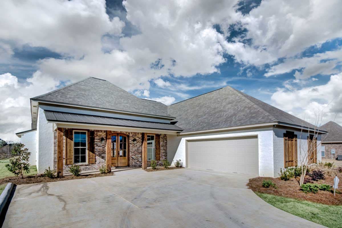 House plan exterior. One-story house with a brick and white painted facade, gabled roof, and attached garage. A covered porch with wooden beams.