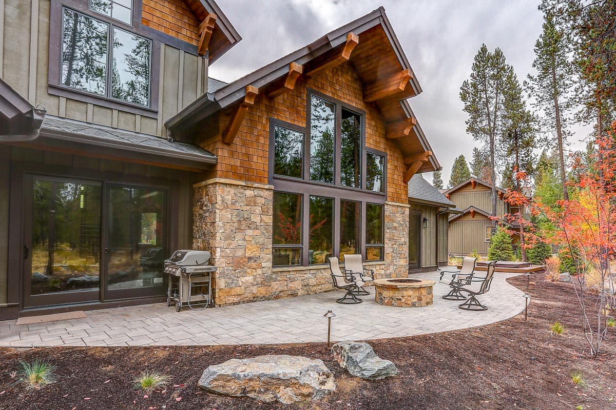 Modern mountain style house exterior with stone and wood siding, large windows, and a patio with fire pit.
