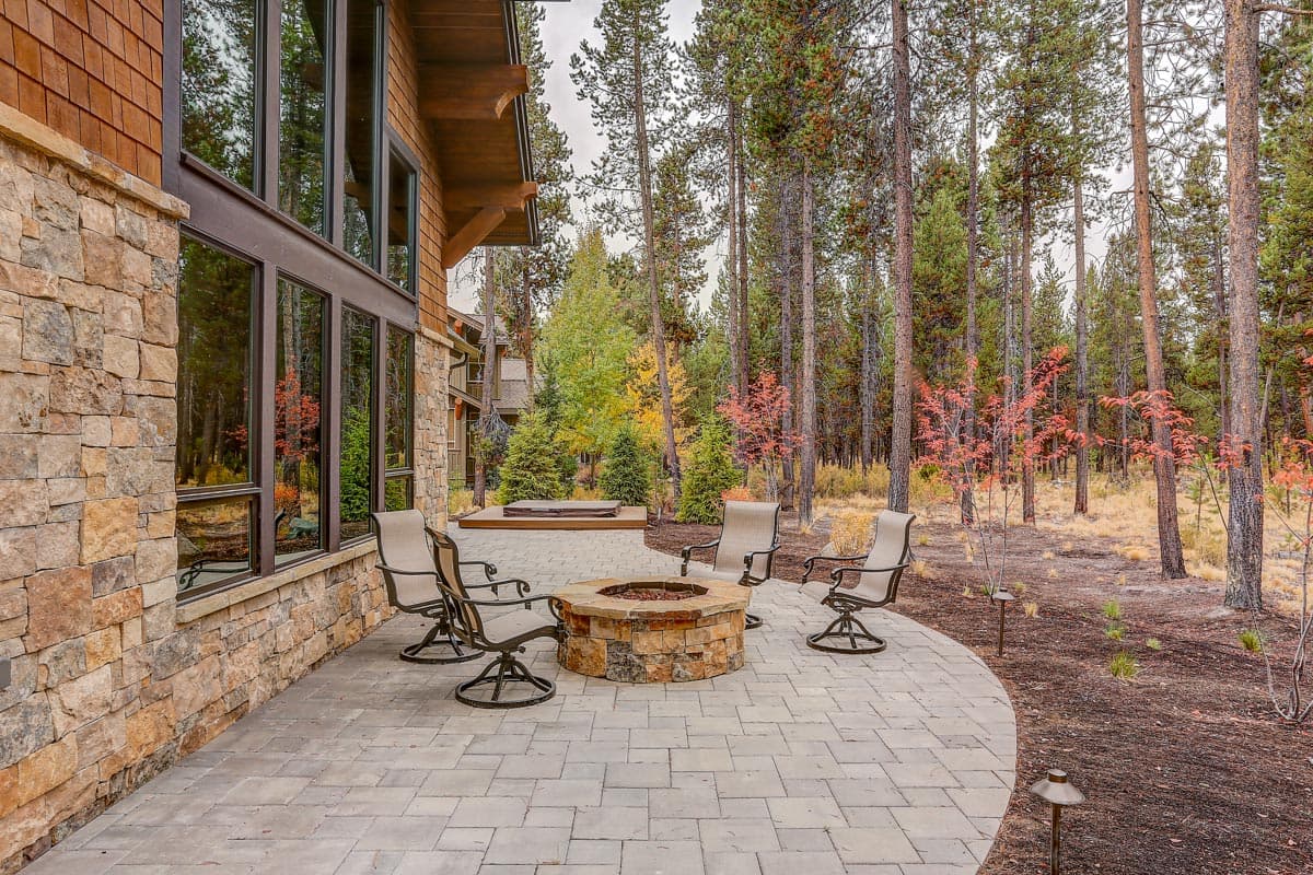 House plan exterior featuring stone and wood siding, large windows, patio with fire pit, and hot tub.
