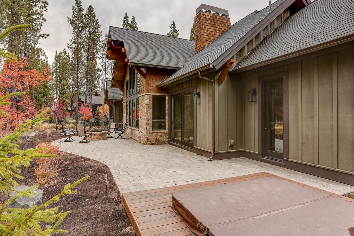 House plan exterior with stone and wood siding, large windows, gables, and a covered porch with hot tub.
