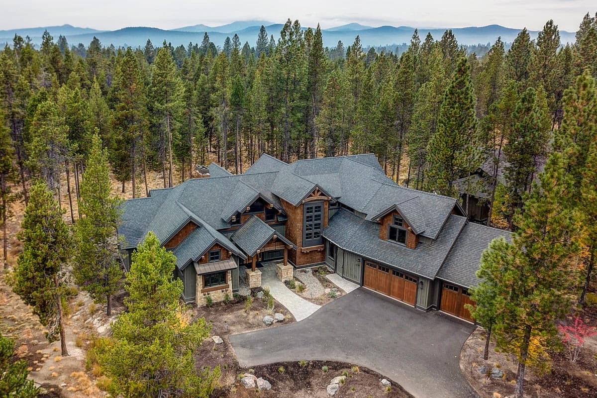 Modern mountain house plan exterior with multiple gables, stone accents, wood siding, and attached three-car garage.