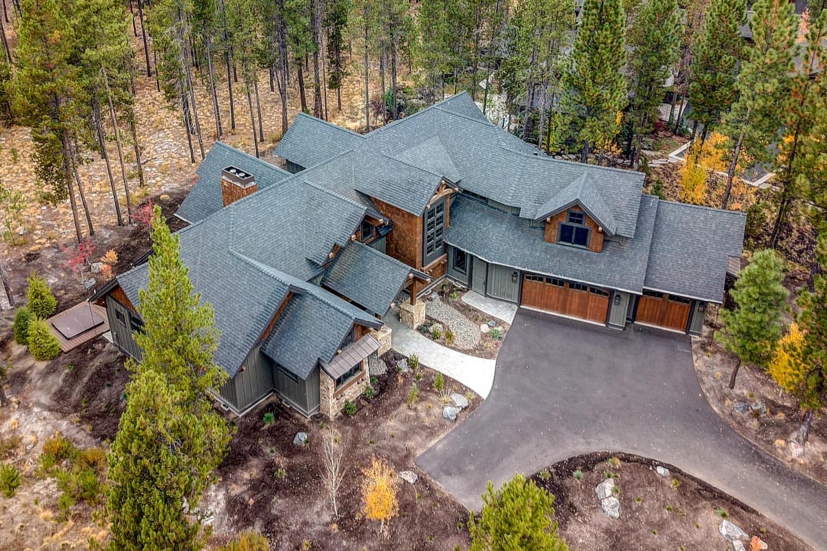 House plan exterior: Modern lodge style, complex rooflines, stone accents, multiple dormers, and a three-car garage.