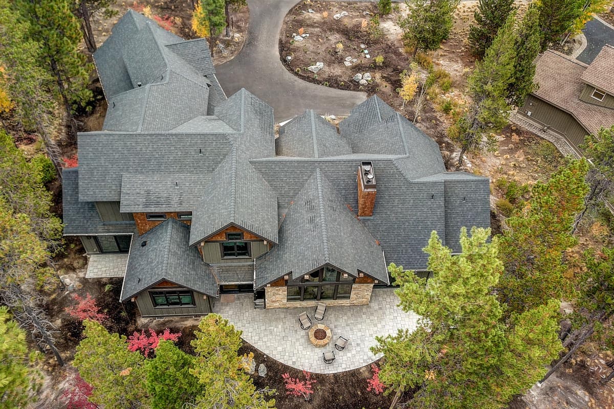 House plan exterior with multiple gables, dormers, prominent chimney, and large stone patio with fire pit.