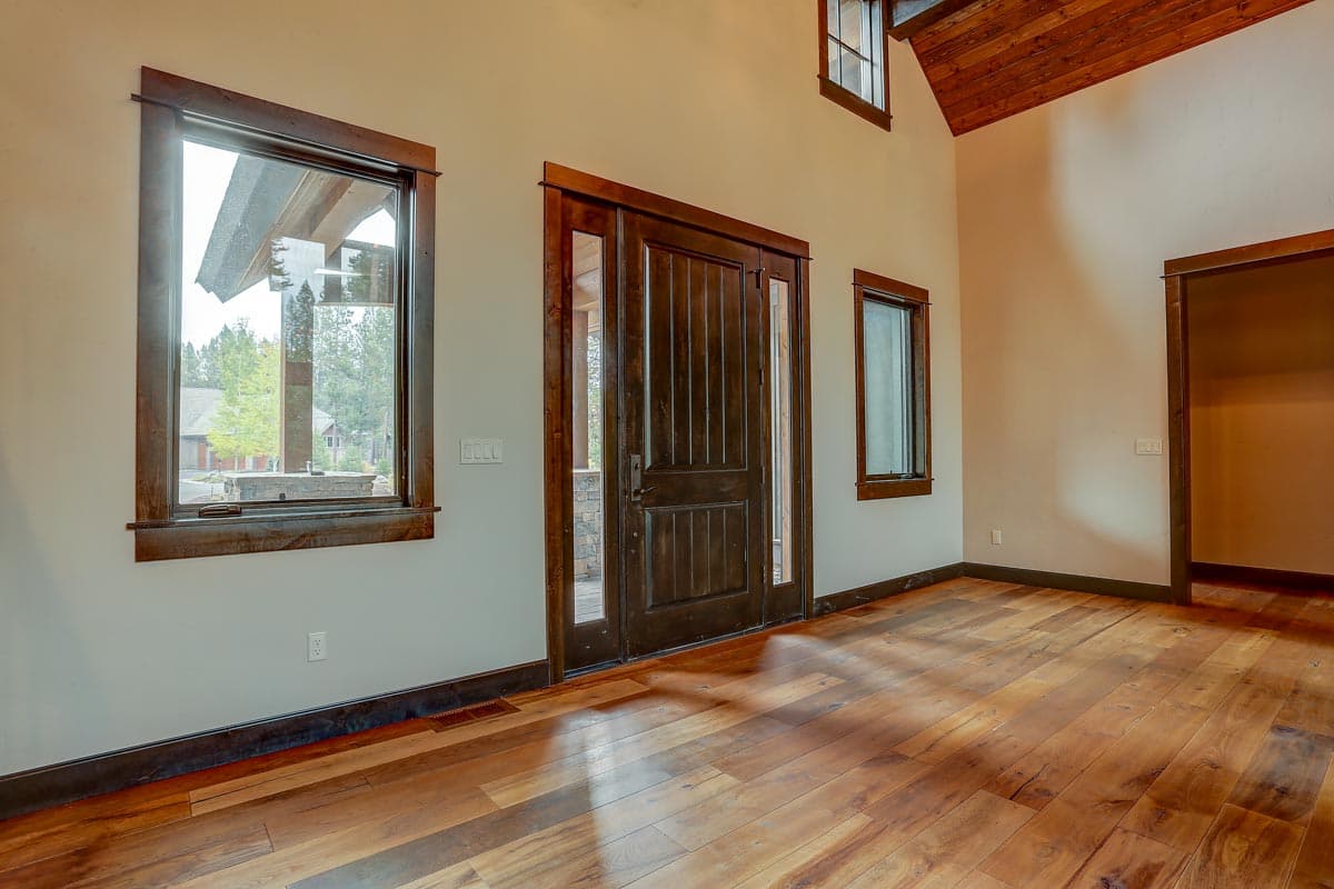 Interior view of entryway with knotty pine vaulted ceiling, dark wood door and trim, and large windows.