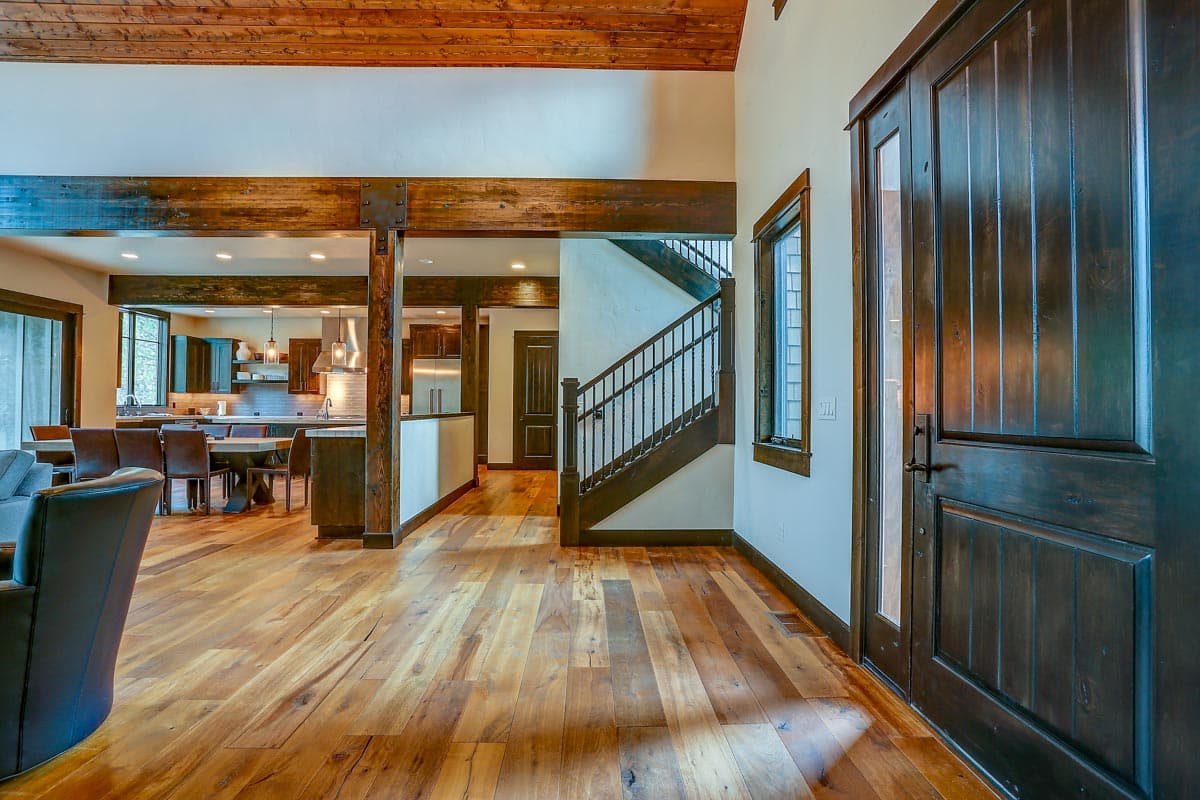 Interior view showing a great room with exposed wooden beams, a staircase, and an open kitchen area with dark cabinets.