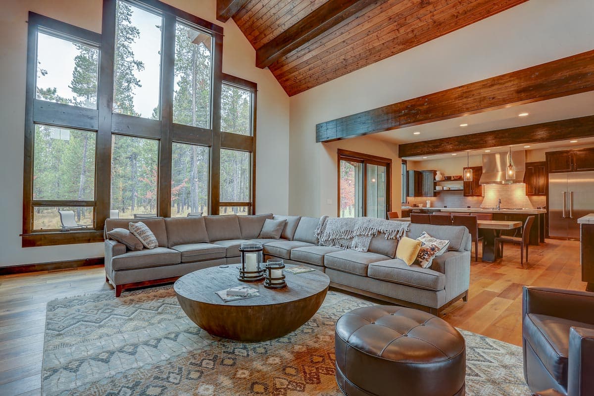 Great room with vaulted wood-beam ceiling, sectional sofa, large round coffee table, and adjacent kitchen with island.