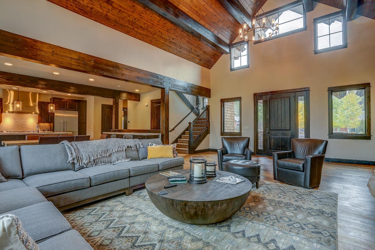Great room with vaulted wood beam ceiling, large sectional sofa, leather chairs, stone-look coffee table, and open view to kitchen.