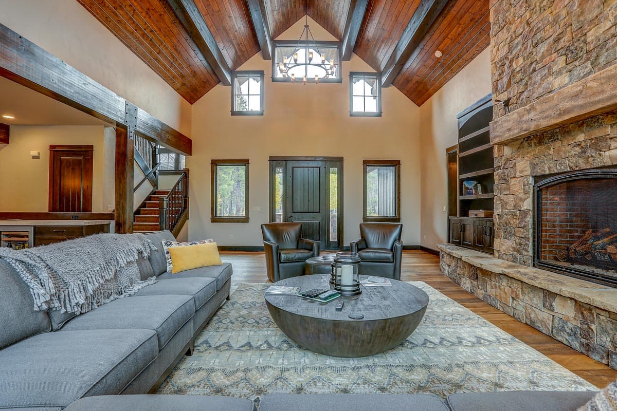 Great room with vaulted, beamed ceiling, stone fireplace, built-in shelving, and large windows.