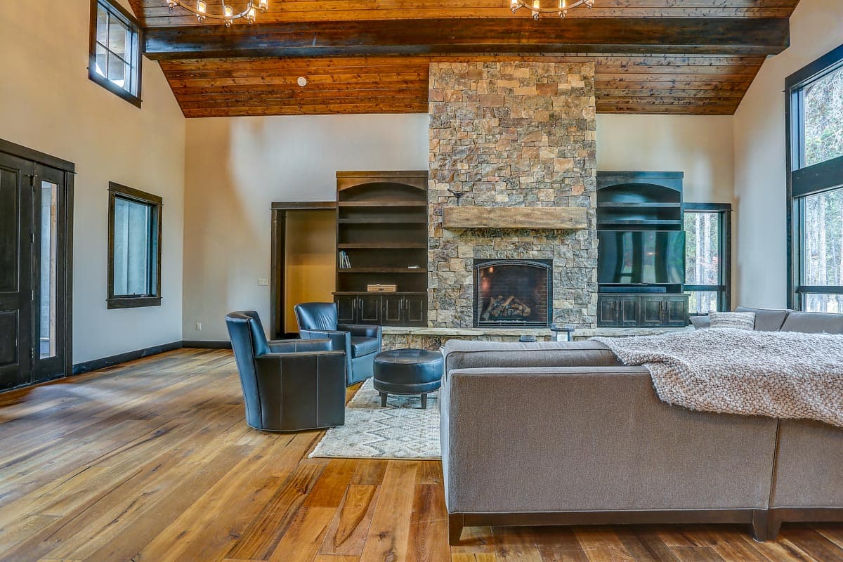 Living room with vaulted wood-beamed ceiling, stone fireplace, built-in shelving, and large windows.