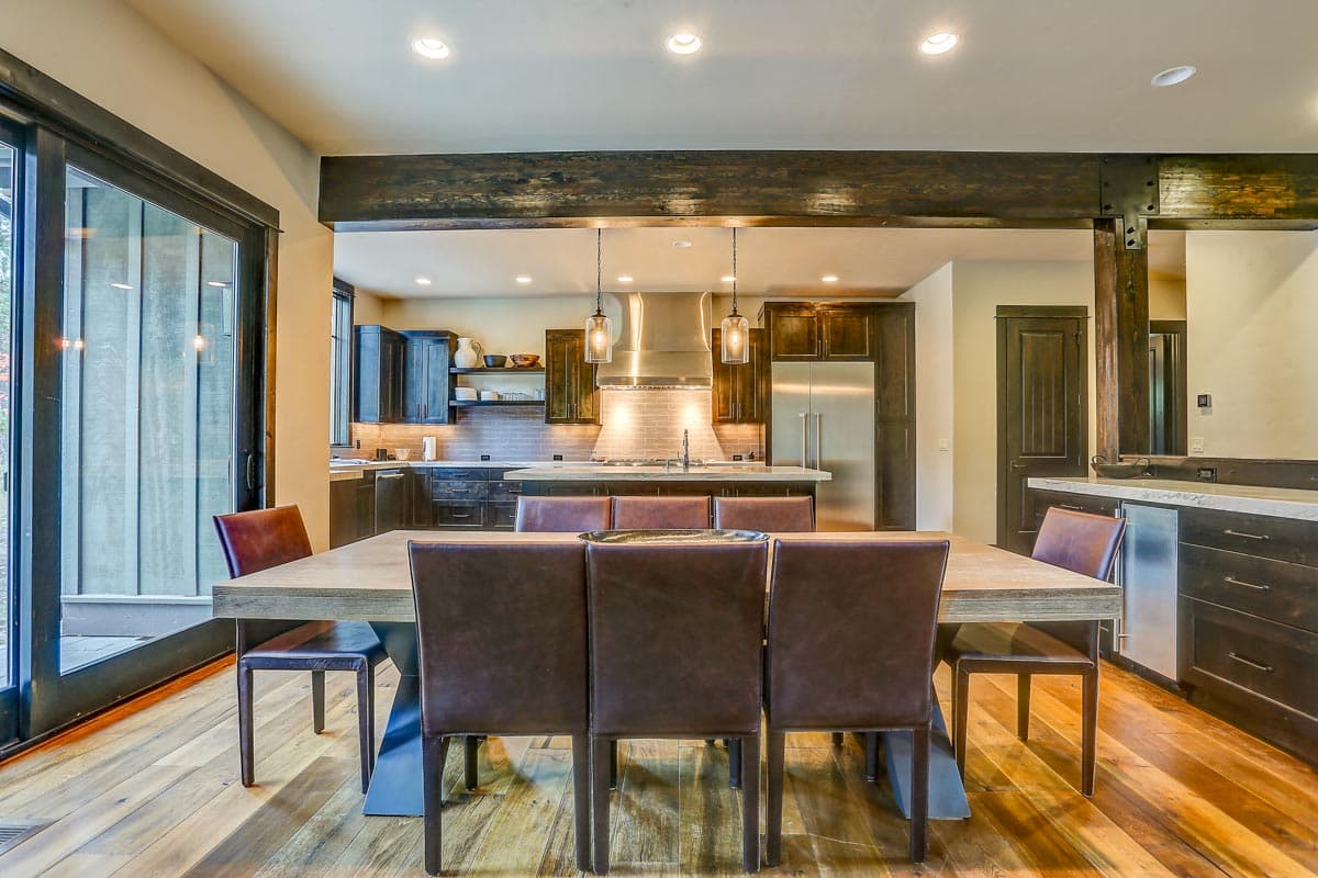 Interior view of dining area and kitchen with island, stainless steel range hood, dark wood cabinetry, and large sliding glass door.