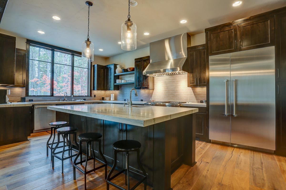 Kitchen with large island, stainless steel appliances, range hood, dark cabinetry, and wood flooring.