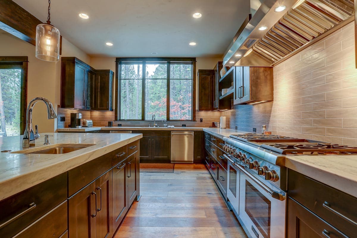 Kitchen with dark wood cabinets, marble island, professional range, and large window overlooking trees.