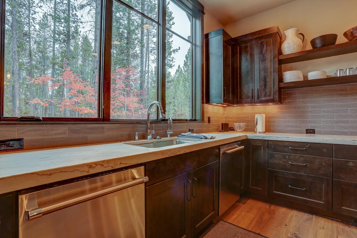 Kitchen with dark wood cabinets, stainless steel appliances, and a large window overlooking trees.