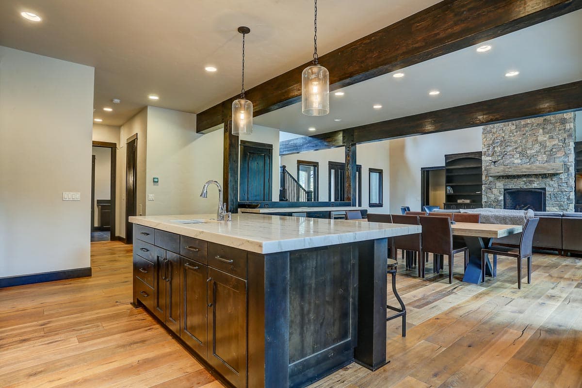 Kitchen island with stone countertop, dark wood cabinets, and pendant lights connects to dining area with stone fireplace and built-in shelving.