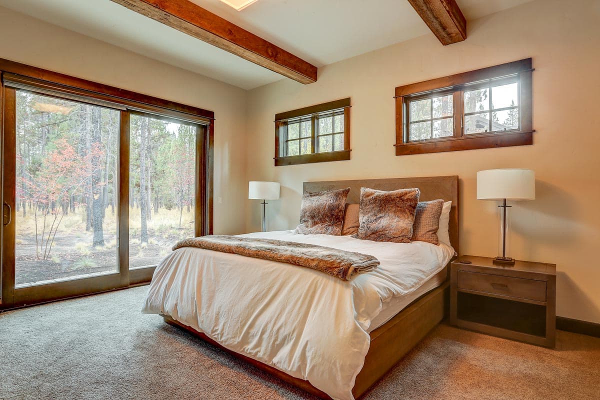 Bedroom interior with wood-framed sliding glass door, two windows, and exposed wooden ceiling beams.