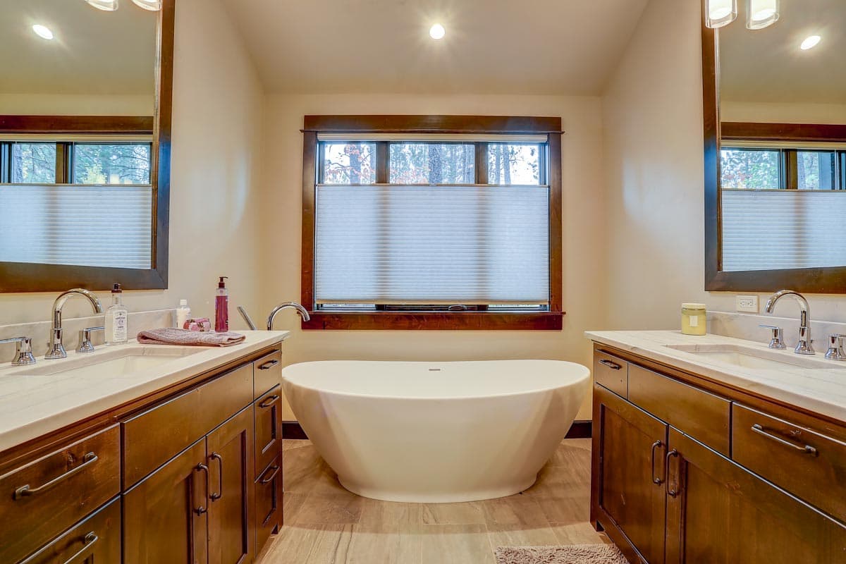 Bathroom with double vanity, freestanding tub, and window overlooking trees.