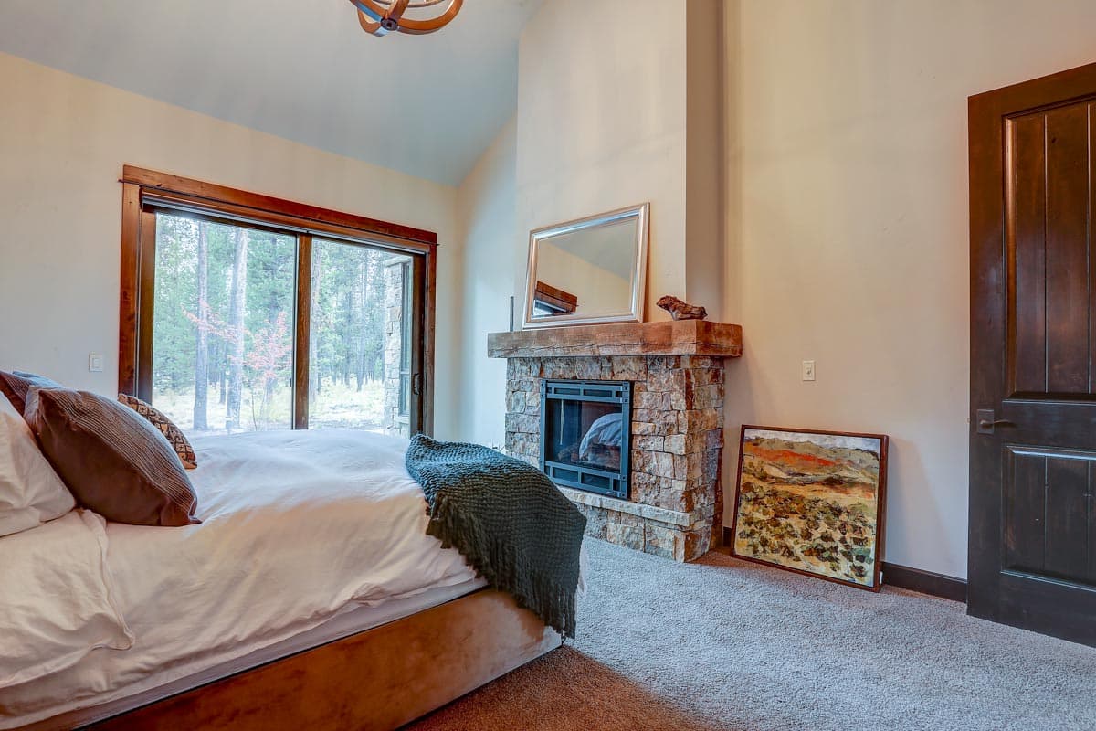 Bedroom with stone fireplace, vaulted ceiling, large sliding glass door, and dark wood door.