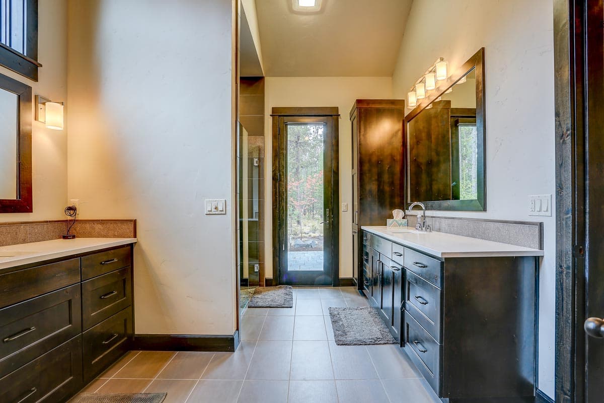 Bathroom interior with double vanity, dark wood cabinets, stone countertop, and glass door to exterior.