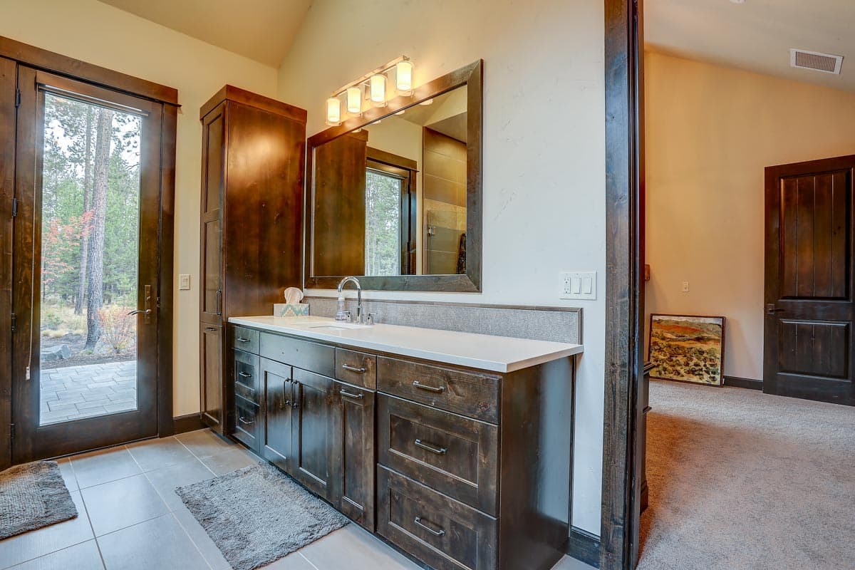 Bathroom vanity with dark wood cabinets, white countertop, and large mirror. Double doors lead outside.