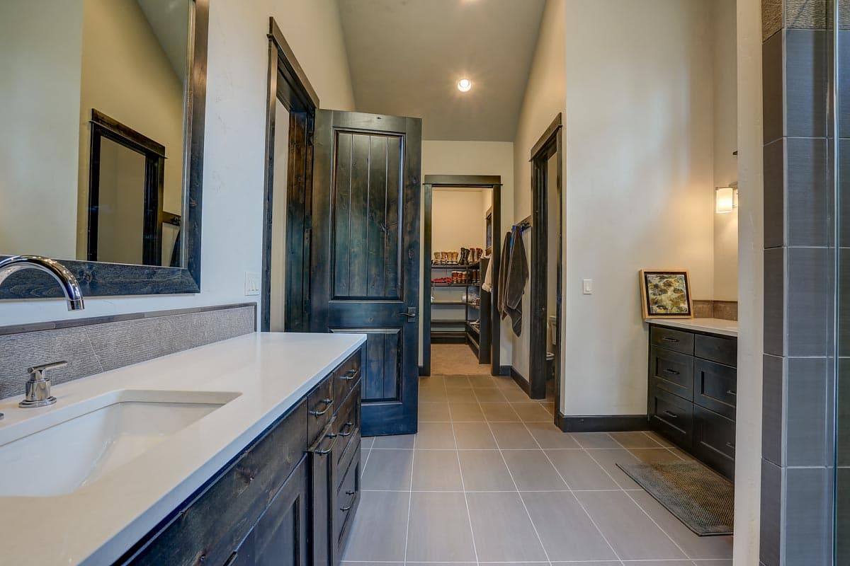 Bathroom with double vanity, walk-in closet visible through doorway, dark wood doors, and tile flooring.