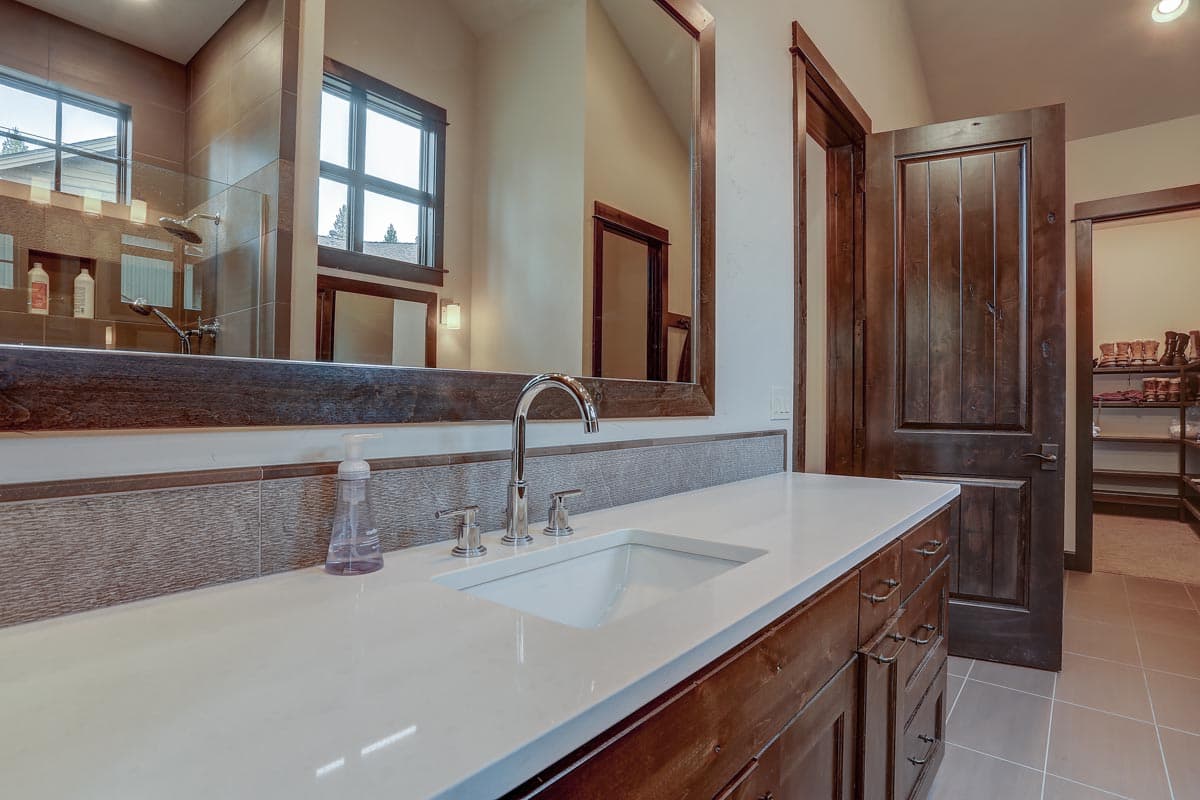 Bathroom vanity with white countertop, wood cabinets, and nickel faucet, adjacent to wood door and walk-in closet.