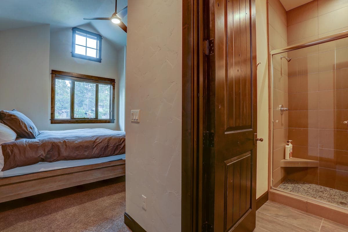 Bedroom with vaulted ceiling and large windows; adjacent glass-enclosed shower with tiled walls.