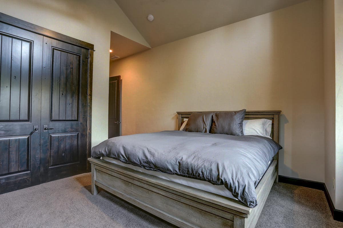 Bedroom with vaulted ceiling, large paneled closet doors, and a wooden bed frame with gray bedding.