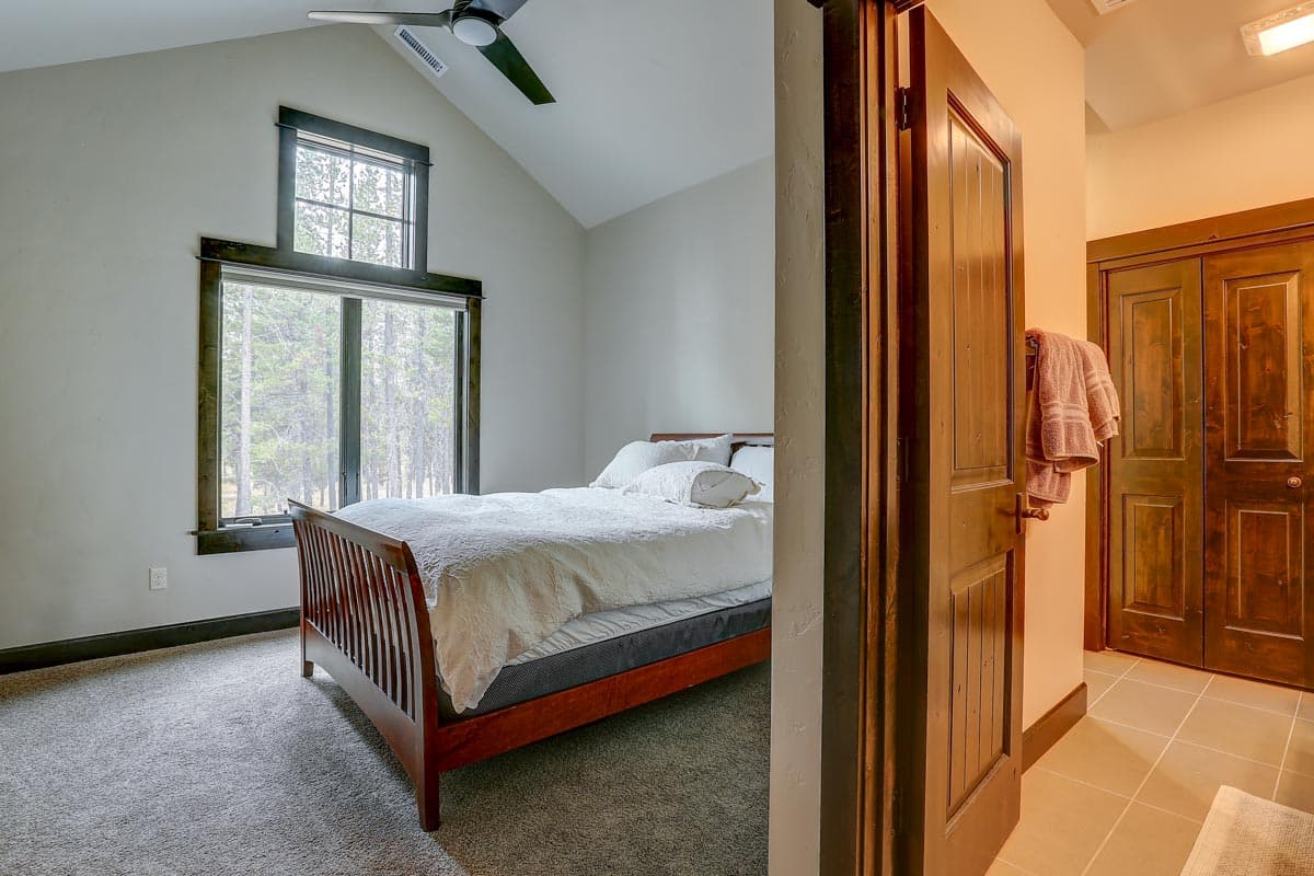 Bedroom with vaulted ceiling, large window, ceiling fan, and wooden door leading to closet with double doors.