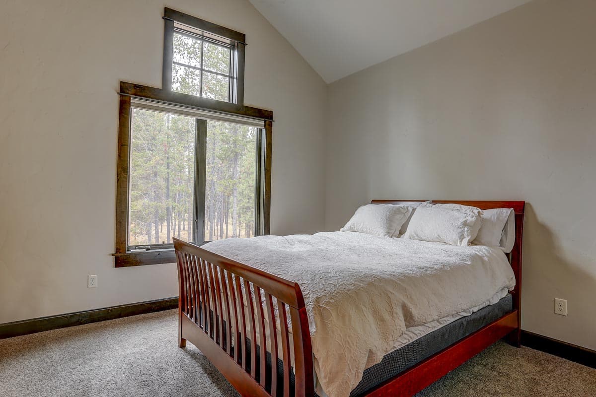Bedroom with vaulted ceiling, large window with forest view, and wooden sleigh bed.