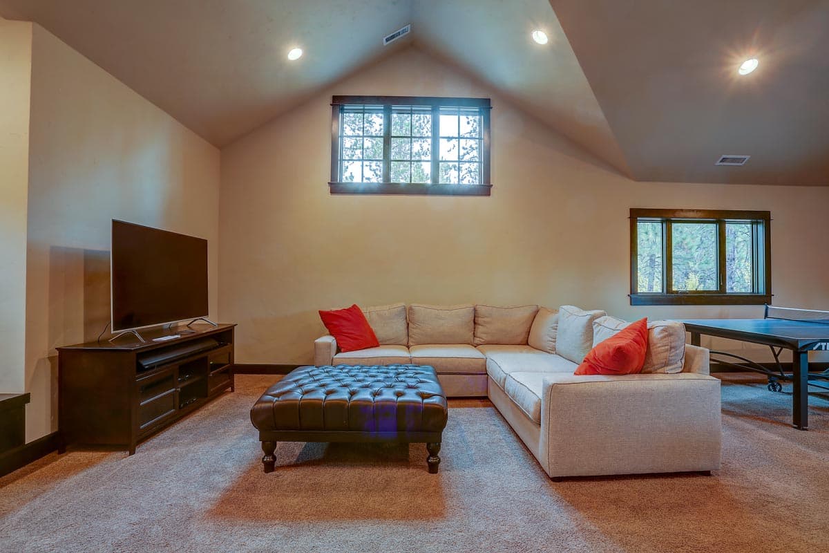 Living area with sectional sofa, ottoman, entertainment center, and ping pong table. Sloped ceiling with dormer window.