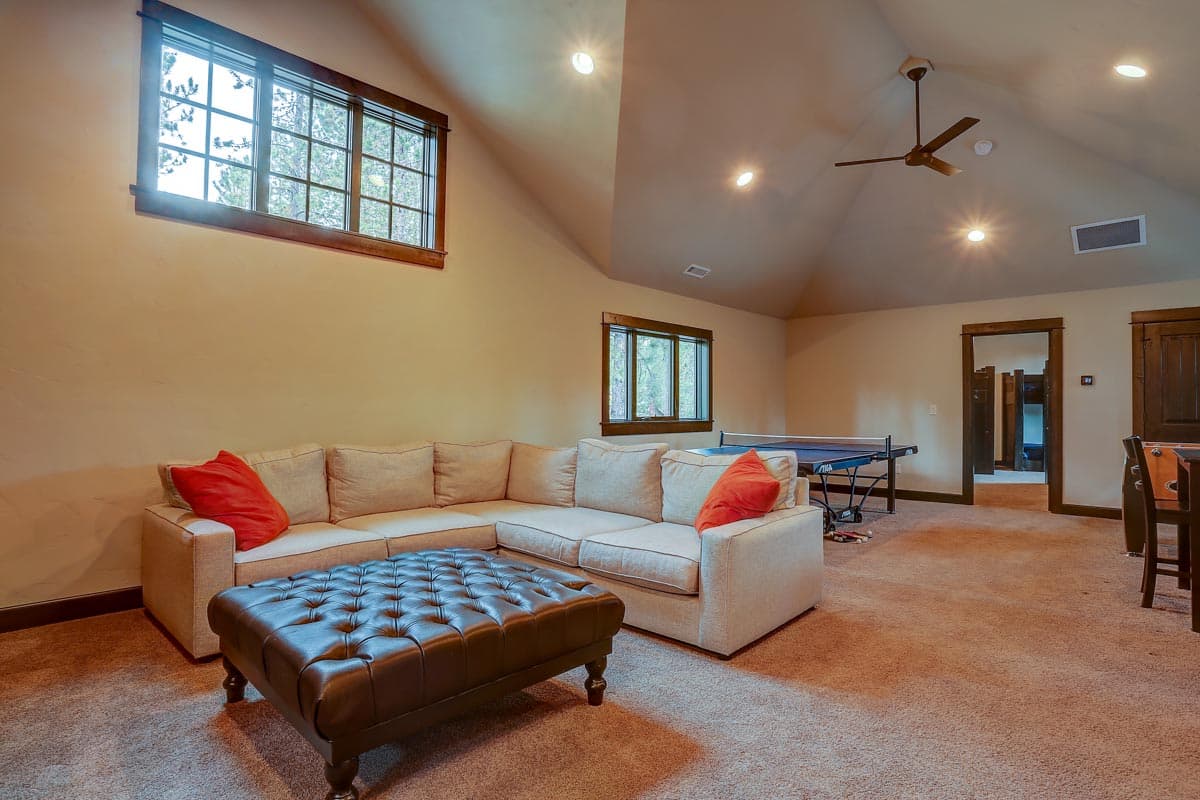 Interior view of a finished basement rec room with a sectional sofa, ottoman, ping pong table, and vaulted ceiling.