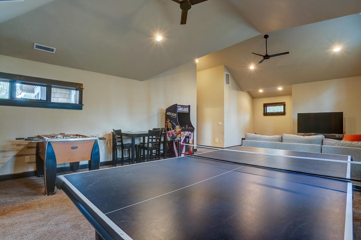 Interior view of recreation room with ping pong table, foosball, arcade game, dining set, sectional sofa, and television.