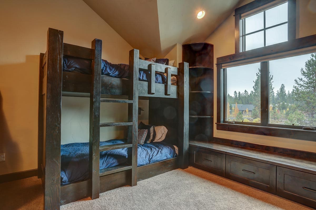 Interior view of a bedroom with dark wood bunk beds, built-in shelving, and a large window with a bench seat.
