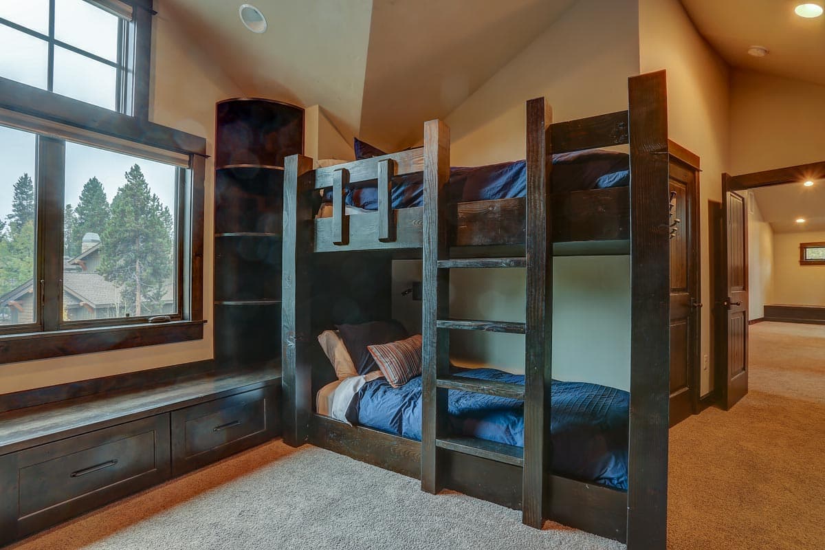 Bedroom with dark wood bunk beds, built-in window seat with drawers, and large window overlooking trees.