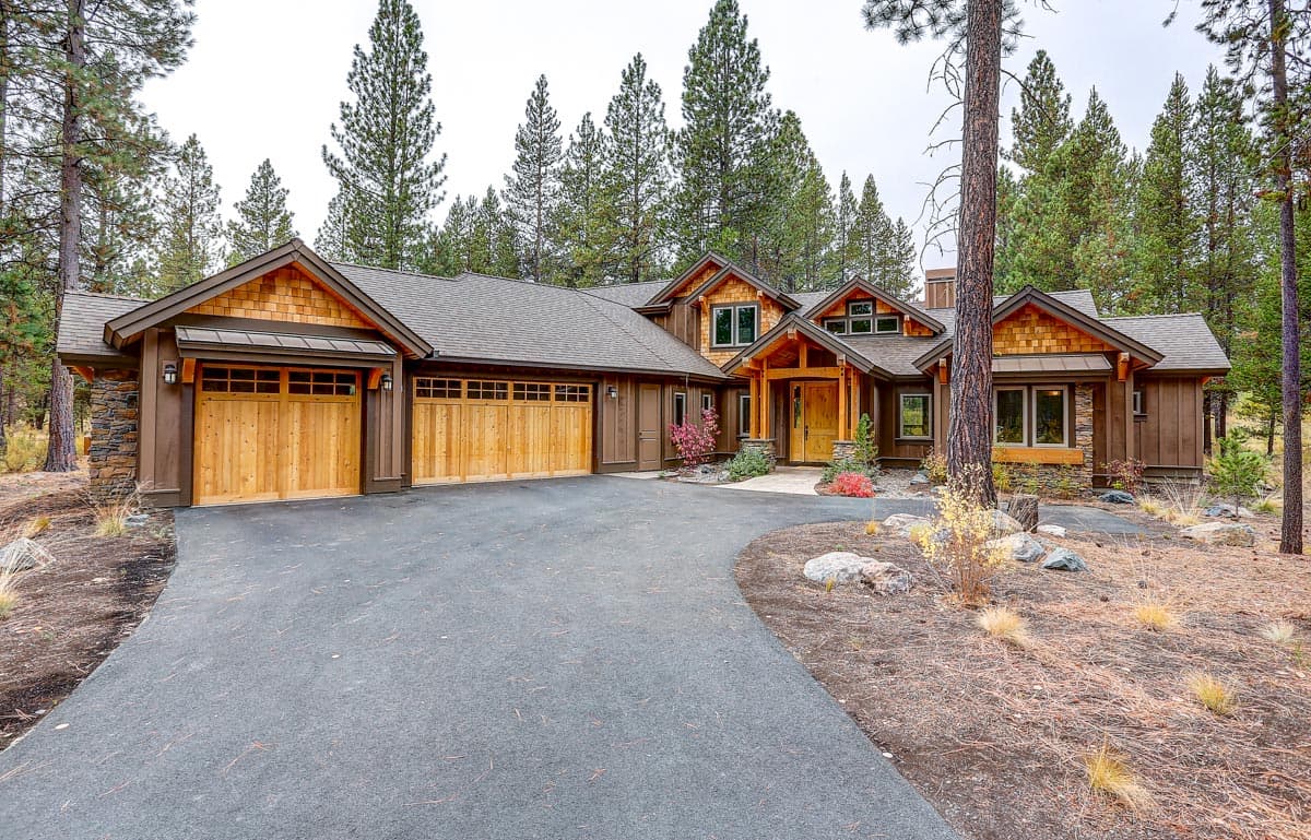 House plan exterior featuring a rustic wood and stone facade, three-car garage, and prominent gabled dormers.