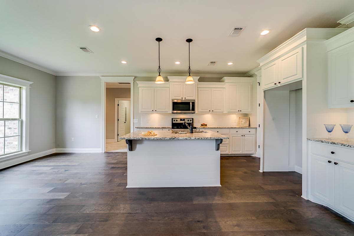 Kitchen with white shaker cabinets, granite countertops, island with pendant lights, and dark wood floors.