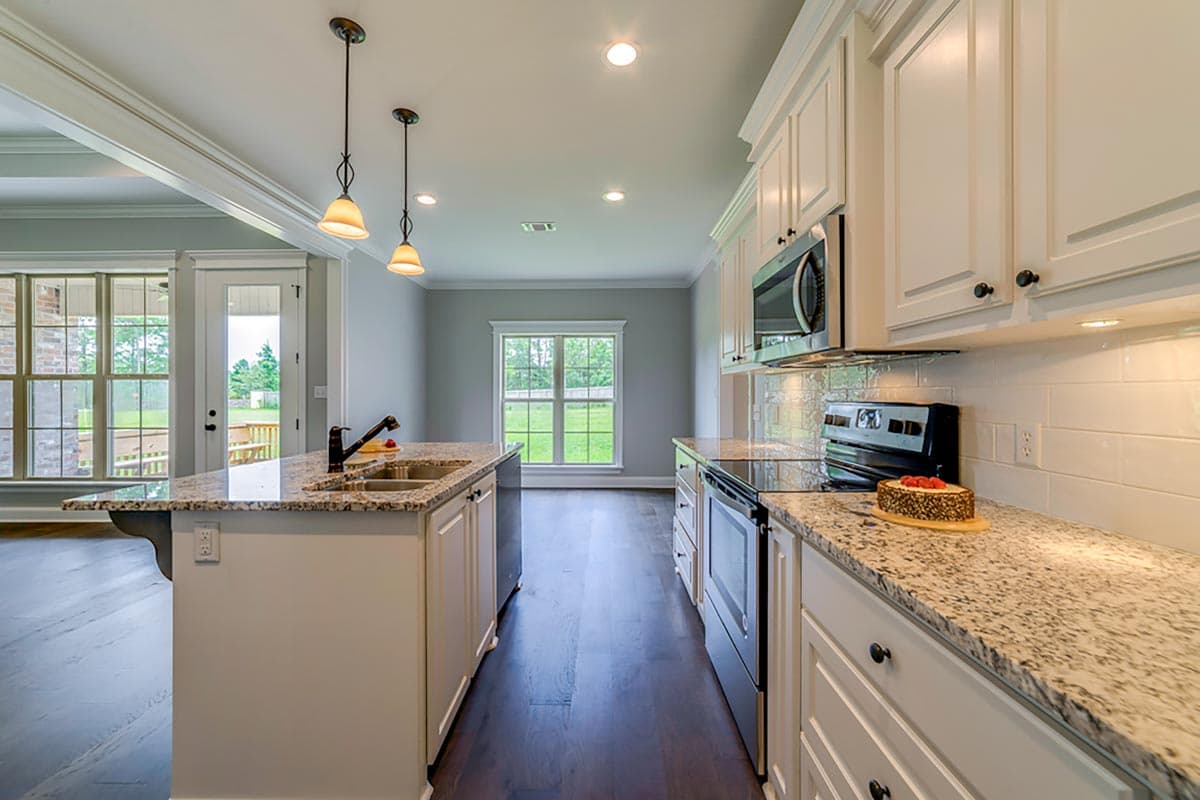 Kitchen with granite countertops, a central island with sink, white cabinets, stainless steel appliances, and pendant lighting.