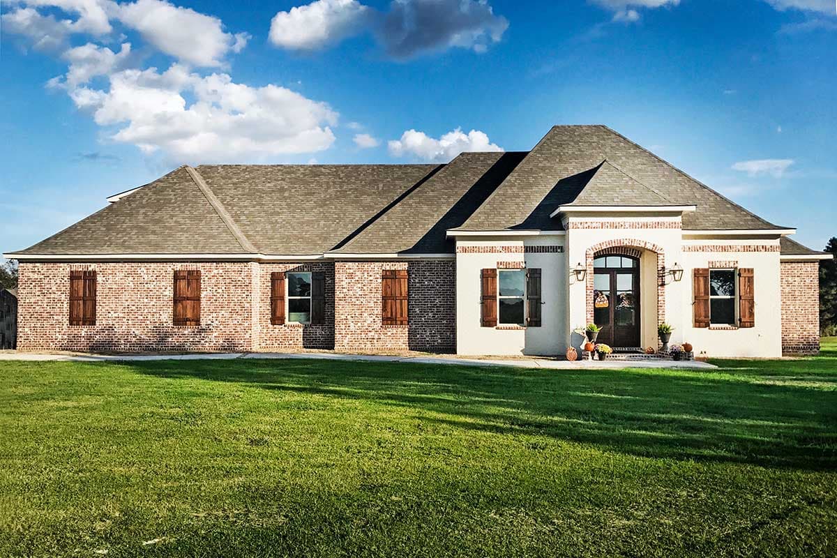 House plan exterior. One-story Ranch style home with brick and stucco facade, gabled roof, and decorative shutters.