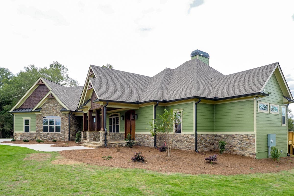 House plan exterior with stone and green siding, covered porch with wood posts, multiple gables and stone accents.