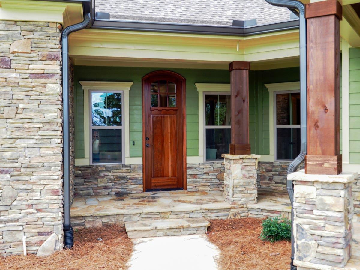 House plan exterior with stone accents, wood front door, large wood columns supporting a covered porch with gabled roof.