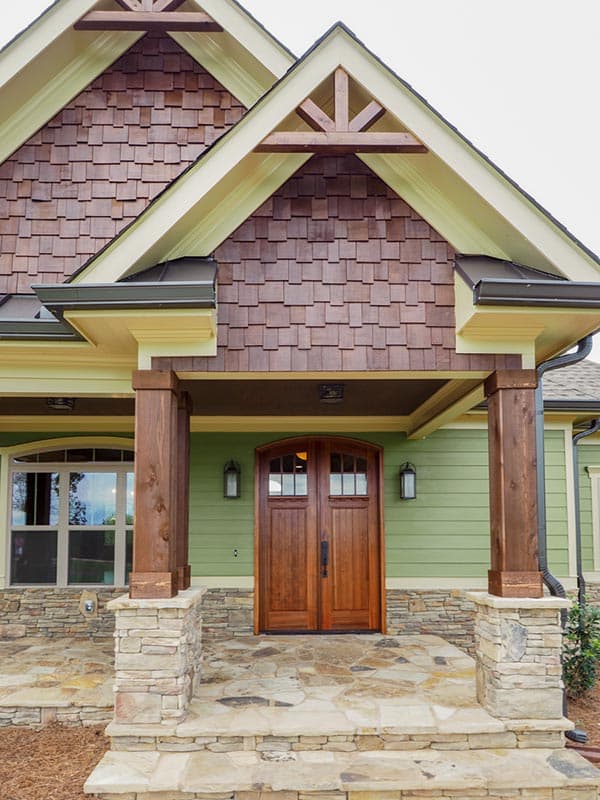 House plan exterior: Craftsman style, double wooden doors with arched transoms, stone accents, and cedar shake gables.