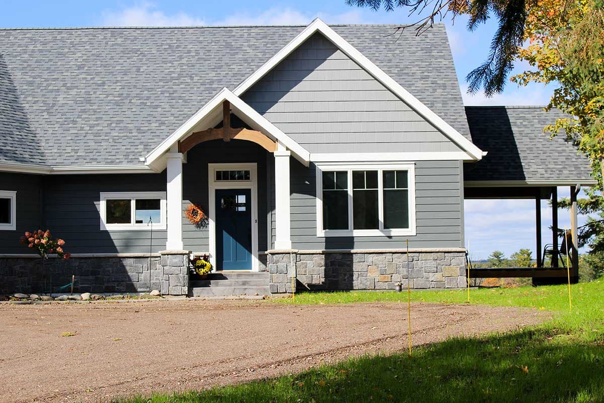 House plan exterior of a one-story home with stone foundation, prominent gable with timber accent over the entryway, and attached covered porch.