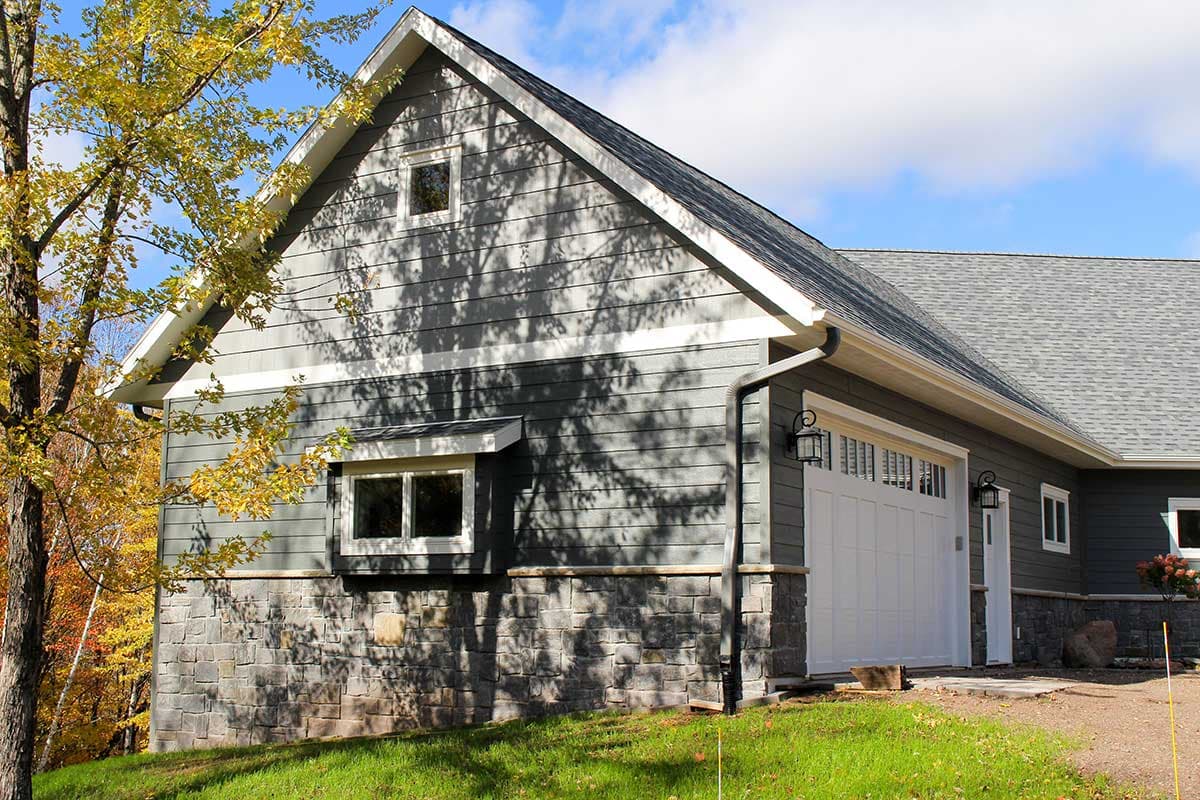House plan exterior: Two-story home with stone base, horizontal siding, gabled roof, and a white garage door.