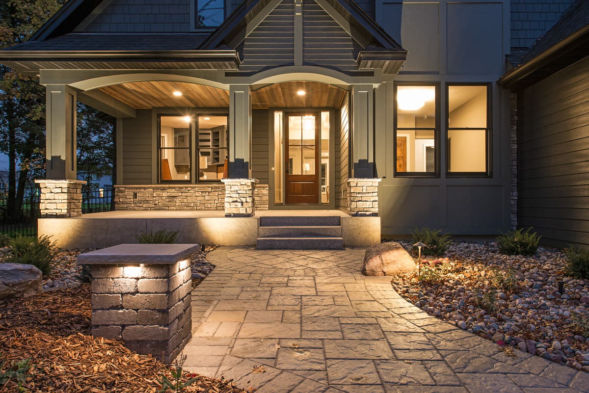 Modern farmhouse exterior with stone-clad pillars, wood-paneled covered porch, and multi-pane entry door.
