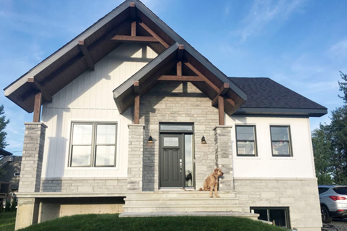 House plan exterior: Two-story modern house with stone and vertical siding, prominent gables, exposed timber framing, and a covered entry.