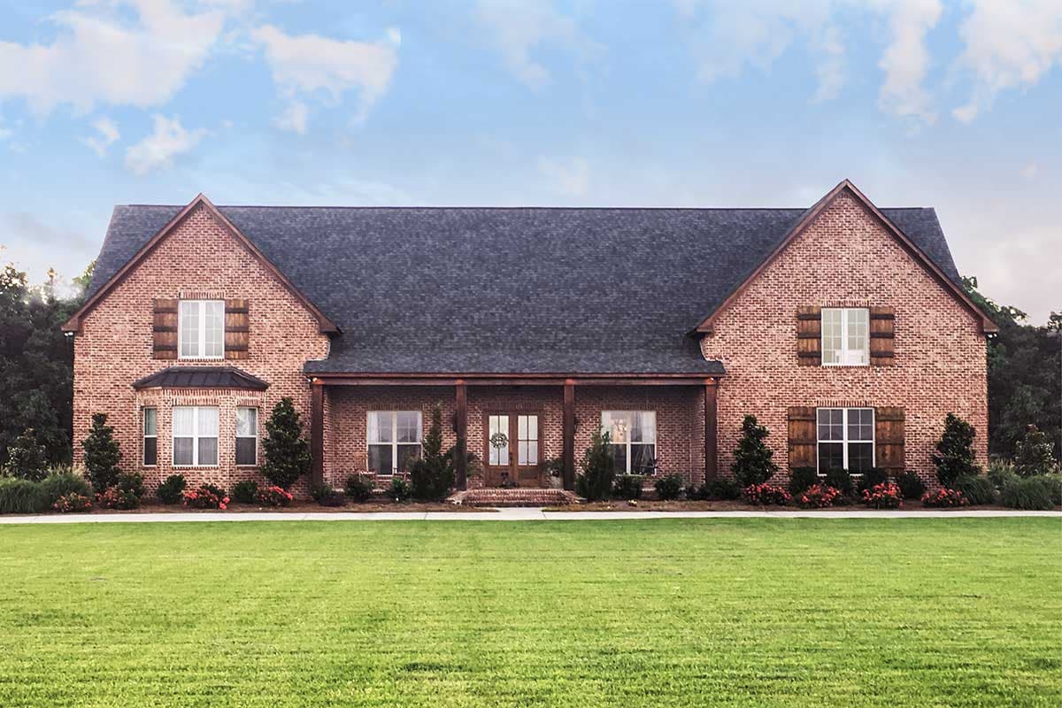 House plan exterior. Two-story brick home with gabled roof, covered porch, and window shutters. Features include a bay window and symmetrical design.