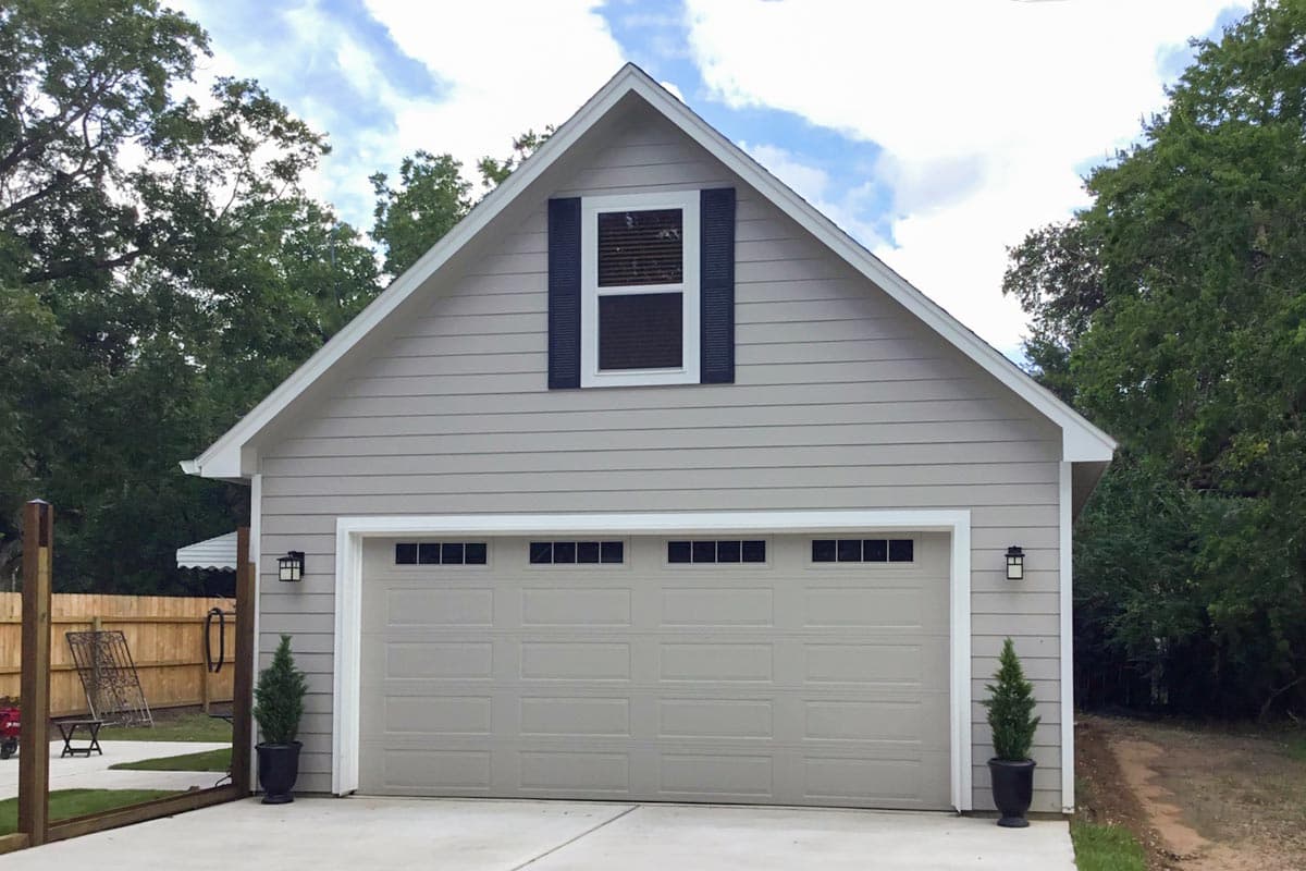 House plan exterior. Two-story structure with gable roof. Includes a garage with carriage-style door and a dormer window with shutters.