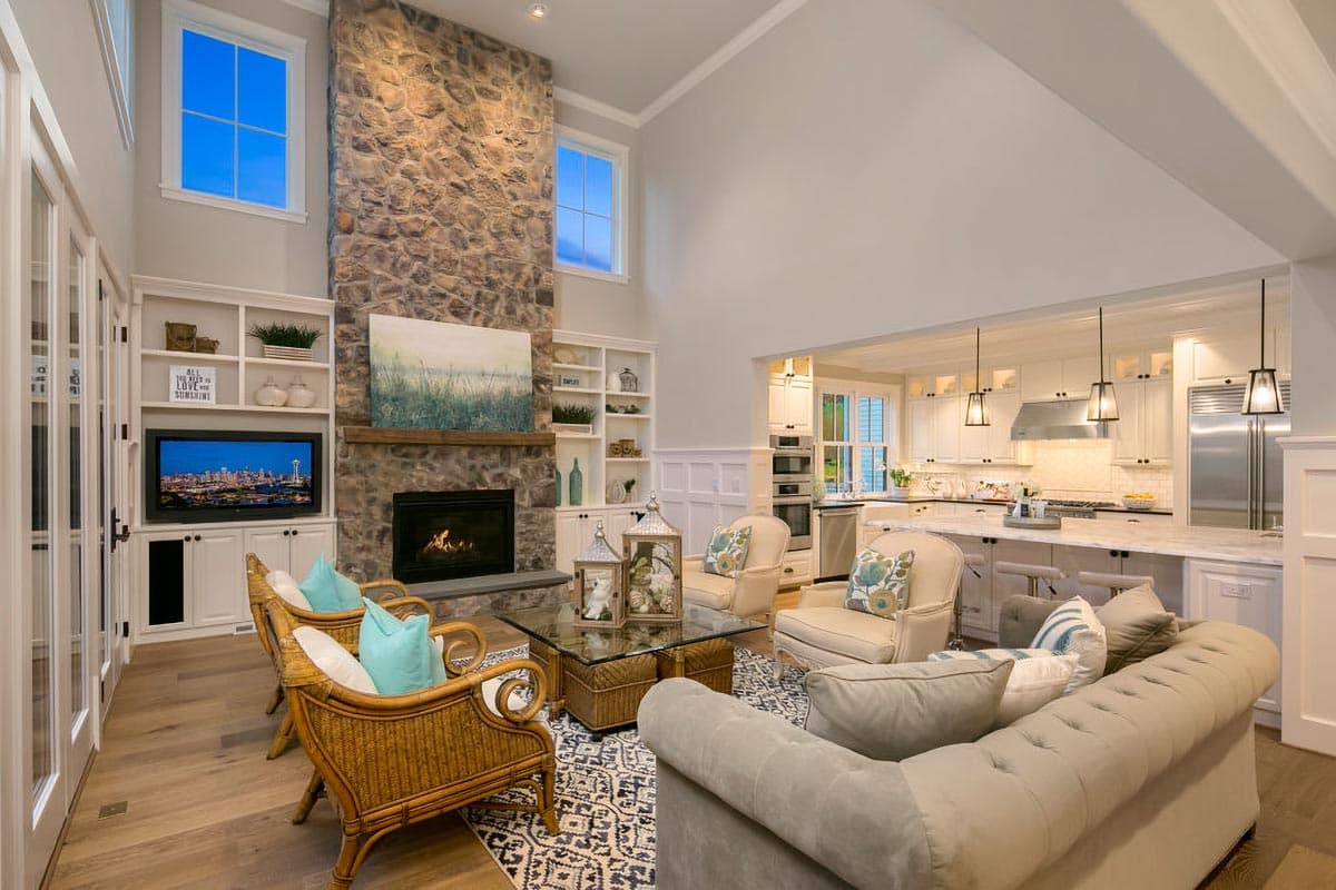 Living room with vaulted ceiling, stone fireplace, built-in entertainment center, and adjacent kitchen with island.