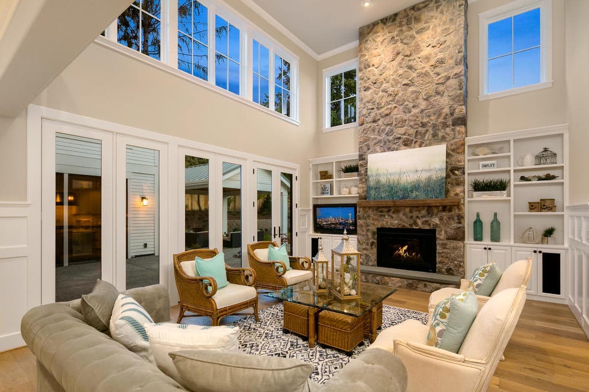 Interior view of living room with stone fireplace, built-in shelving, large windows, and double doors leading outdoors.